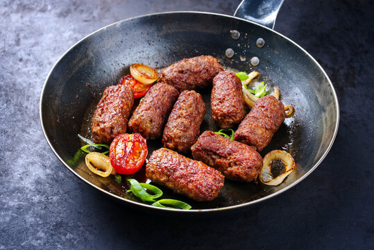 Traditional Croatian cevapi spicy meat ball rolls with tomatoes and onion rings served as close-up in a skillet