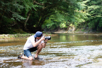 渓流で一眼レフカメラを構える男性