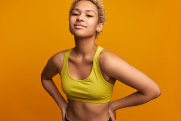Beautiful young slim curly haired mixed-race blondie with nose ring posing against orange wall in...