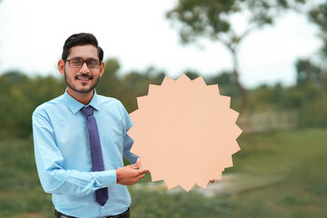 Young indian banker or officer showing blank board on nature background.