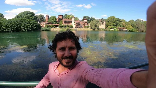 happy tourist visiting Turin (Torino), piedmont, Italy. Happy man take selfi photo with Borgo Medieval village and fortress of Turin and river Po. Fisheye lens 
