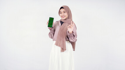 Young woman in hijab showing cellphone screen and okay isolated on white background