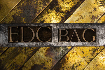 EDC Bag text formed with real authentic typeset letters on vintage textured silver grunge copper and gold background