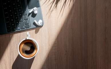 top view computer keyboard, cup of coffee and earphone on wooden table with sunlight in the morning.