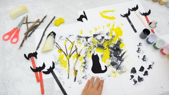 Child making card for the holiday  Halloween. Funny crafts from paper, natural tree twigs and painting with a sponge. The concept for Halloween. DIY. Children's art project, a craft for children.