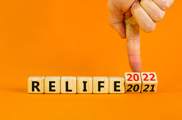 Planning 2022 relife new year symbol. Businessman turns wooden cubes and changes words 'relife 2021' to 'relife 2022'. Beautiful orange background, copy space. Business, 2022 relife new year concept.