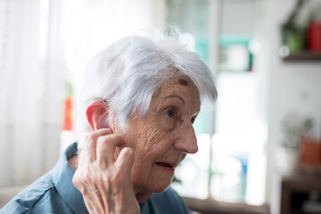 Close up of serious senior gray-haired Caucasian woman adjusting her in-ear hearing aid kit