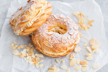 French traditional cake Paris Brest with praline cream, powdered sugar and almond petals on top on a gray concrete background. Copy space.