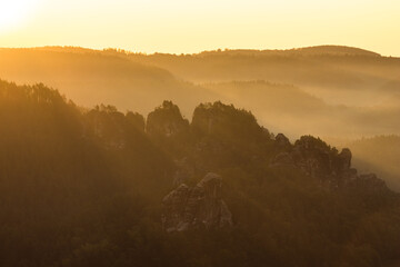 Morning sun shining through foggy landscape with rocks and forest.
