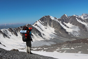 A female hiker with a large trekking backpack admires the view of the mountain range