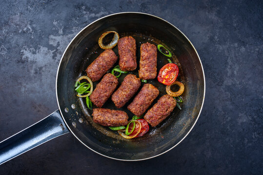 Traditionelle kroatische Cevapi als w&uuml;rzige Fleischb&auml;llchen mit Tomaten und Zwiebelringen, serviert als close-up in einer Bratpfanne 