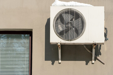 An outdoor air conditioner unit installed on the wall of a residential building next to the window. Installation, repair and maintenance of air conditioning systems in residential premises.