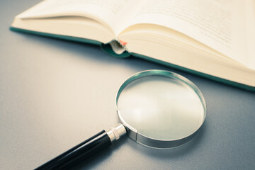 Magnifying glass and opened book - obrazy, fototapety, plakaty
