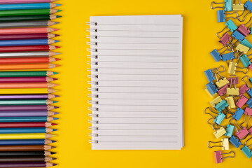 Set of colorful supplies, white blank note pad with color pencils on a yellow background