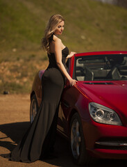 beautiful glamorous girl with white hair in a black elegant long evening dress sits in a convertible