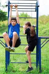 teenage boy and girl exercising outdoors, sports ground in the yard, they posing at the horizontal bar, healthy lifestyle