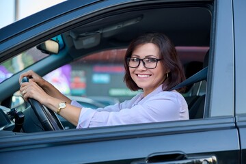 Middle-aged woman driver with glasses, female driving a car.