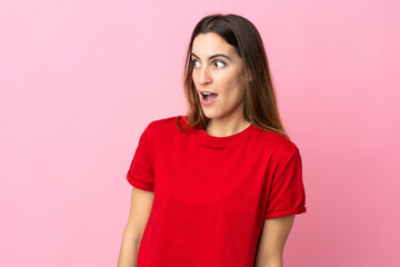Fototapeta premium Young caucasian woman isolated on pink background doing surprise gesture while looking to the side