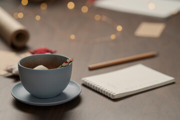 Cup of hot chocolate next to notepad and christmas decorations