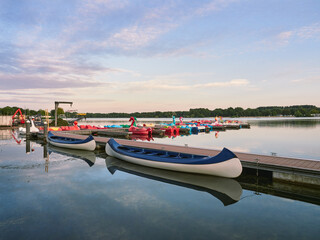 Fototapeta premium A quiet evening at Lake Unterbacher See in German city of Dusseldorf. Moored pedalos nad kayaks for rent. Beautiful landscape before the sunset