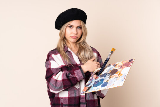 Teenager artist girl holding a palette isolated on blue background feeling upset