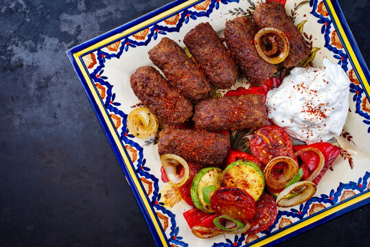 Traditionelle kroatische Cevapi als w&uuml;rzige Fleischb&auml;llchen mit Barbecue Gem&uuml;se und Zaziki serviert als Draufsicht auf einem rustikalen Teller 