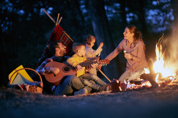 Fototapeta na wymiar A young happy family having a good time around a campfire in the forest