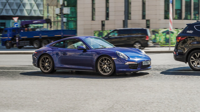 Porsche 911 Carrera 4 in blue color moving on the street. Front side view of shiny sports car rushes in city road