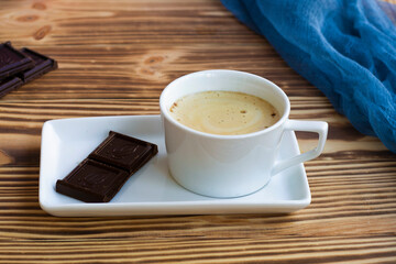 latte with pieces of dark chocolate on a plate. Wooden table and a cup of hot latte. coffee with froth and milk. Coffee drink with dessert. High quality photo