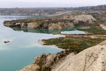 Fototapeta na wymiar Turquoise water in a chalk quarry in Krichev Belarus. Extraction of chalk. Cretaceous quarries against the background of an autumnal forest of green and yellow color with hillocks from reclaimed earth