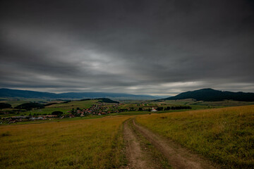 Dirt road leading to a small hungarian village in Transylvania Romania, dark thick rain clouds in the background.