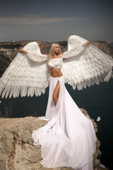 Young beautiful woman fallen sad angel sits on the sea beach. Creative sexy costume, huge...