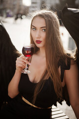 black fallen angel. beautiful girl in a black evening dress with black wings in the wheelhouse a glass of wine © olenakucher