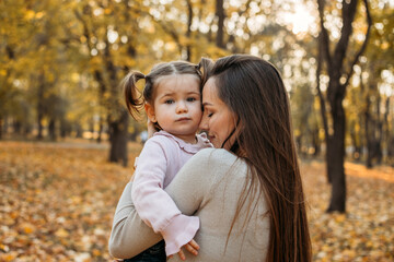 Ways to Carry a Toddler. Close up outdoors portrait of Happy family mom and toddler baby girl in fall park. Little girl and her mother in the autumn park.