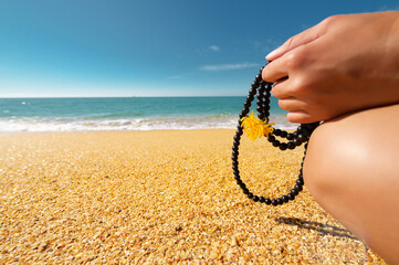 The hand of a white woman holds a rosary for the practice of prayer and meditation on the background of the sandy coast of the sea and sky. Outdoor meditation