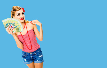 Photo of happy smiling woman with money, euro cash banknotes, dressed in pin up style, over bright blue color background with copy space area. Caucasian blond girl in retro fashion and vintage concept