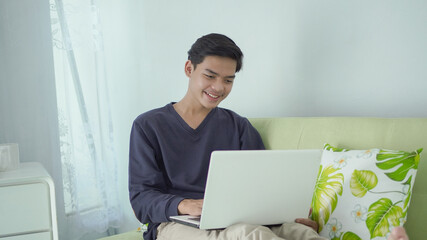 handsome asian man enjoying at home looking at his laptop screen