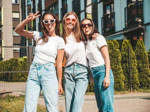 Three young beautiful smiling hipster female in trendy summer same clothes. Sexy carefree women posing on the street background.Positive models having fun in sunglasses.Hugging. Cheerful and happy