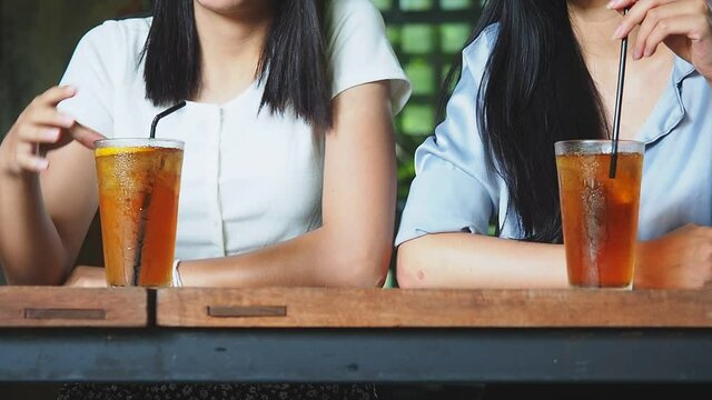 Close up of women drinking ice tea from plastic cup with straw at cafe. Two women discussing in a cafe while having ice coffee.