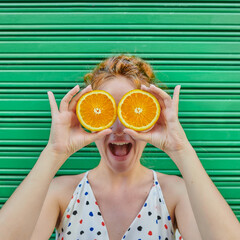 Young woman with orange hair playing with an fresh orange on green background
