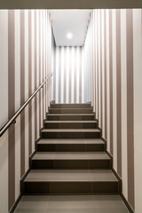 Vertical shot of gloomy lit staircase with vertical dark and white stripes on the walls. Concept for maze, labyrinth, mystery, secret chamber.