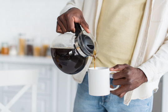 cropped view of african american man holding coffee pot and pouring drink in cup