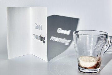 A cup of instant coffee and sugar and a good morning greeting card. Morning shadows on the table.