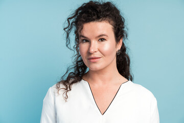 Closeup portrait of perfect middle aged woman with light makeup and curly hair. Emotion and feeling concept. Studio shot, indoor, isolated on light blue background