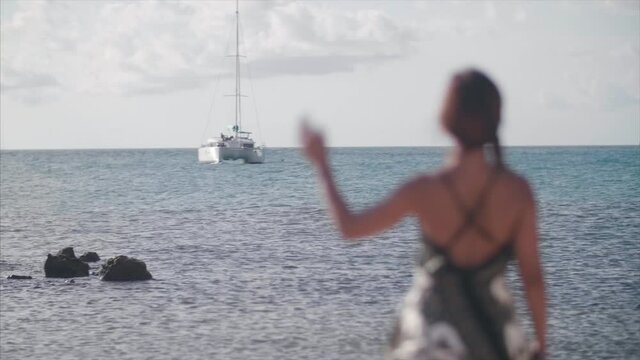 Lady waves at Catamaran from the shore. 