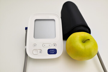 Blood pressure machine and a red apple. Healthy lifestyle concept, blood pressure monitor and an apple on the brown wooden background.