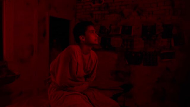 Mad man in straitjacket getting crazy sitting on the bed in the cell of mental hospital and looking in the camera