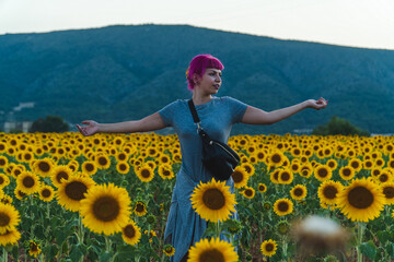 mujer de cabello rosa con los brazos abiertos en medio de un campo de girasoles, mujer con...