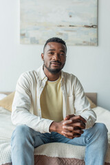 young african american man with clenched hands sitting on bed