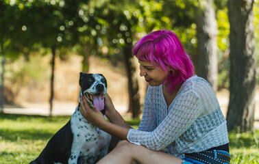 MUJER FELIZ AGARRANDO A  SU PERRO CON AMBAS MANOS EN EL PARQUE, NIÑA DE PELO ROSA MIRANDO A SU...